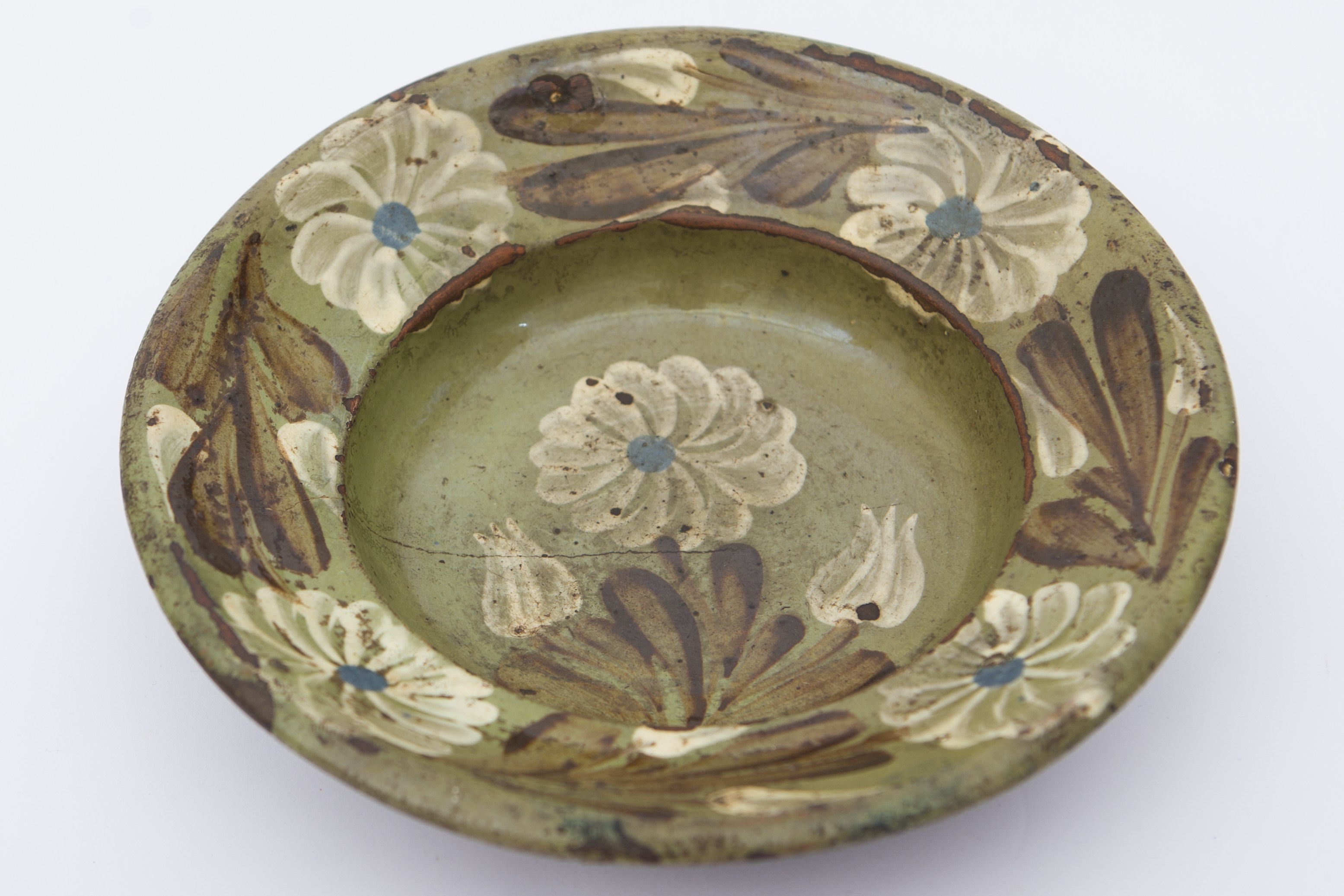 Recipient ceramic, smălțuit în interior, de formă tronconică cu baza plată, pereții puțin ridicați și buza larg evazată. Peste stratul verde de angobă a fost pictat decorul fitomorf stilizat, compus din cinci flori cu petale albe, având câte un punct albastru în mijloc și frunze maro închis. Una dintre flori, încadrată de doi boboci de floare se află pe fundul vasului. Celelalte patru flori sunt dispuse pe marginile vasului în alternanță cu frunze și boboci de floare. Pe spate prezintă o tortiță de mici dimensiuni pentru suspendare. Blidul era folosit pentru servirea hranei sau pentru decorarea interioarelor. Prezintă uzură funcțională. Cromatică: fond: cărămiziu (exterior); verde (interior); motive: maro; alb; albastru.