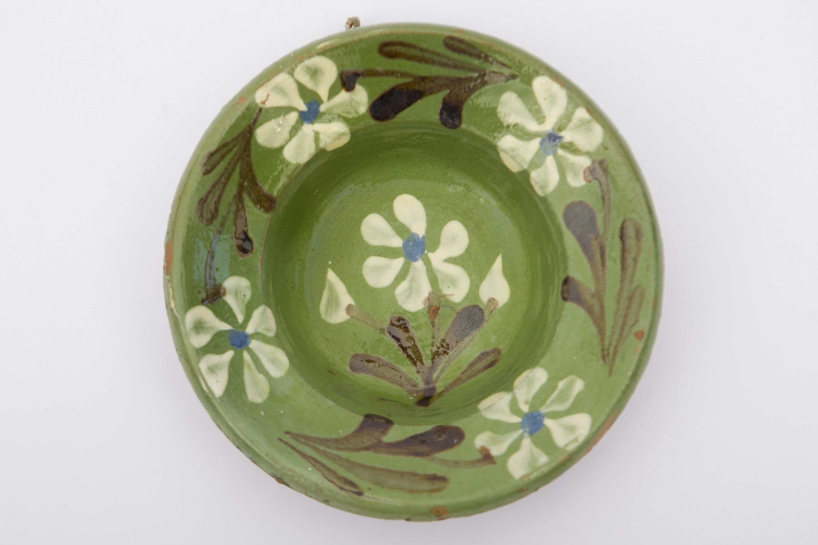 Vas ceramic smălțuit în interior, de formă tronconică, cu baza plată, pereții ușor ridicați și marginea larg evazată. Peste stratul verde de angobă a fost realizat prin pictare, decorul fitomorf stilizat, ilustrând cinci flori cu petale albe, cu câte un punct albastru în mijloc, și frunze negre. O floare încadrată de doi boboci se află pe fundul vasului. Celelalte patru flori sunt dispuse pe marginile vasului în alternanță cu frunze negre. Pe spate prezintă o ”tortiță” de mici dimensiuni pentru suspendare pe perete. Recipientul era folosit pentru servirea hranei, sau decorarea interioarelor. Prezintă uzură funcțională. Cromatică: fond: cărămiziu (exterior); verde (interior); motive: negru; alb; albastru.
