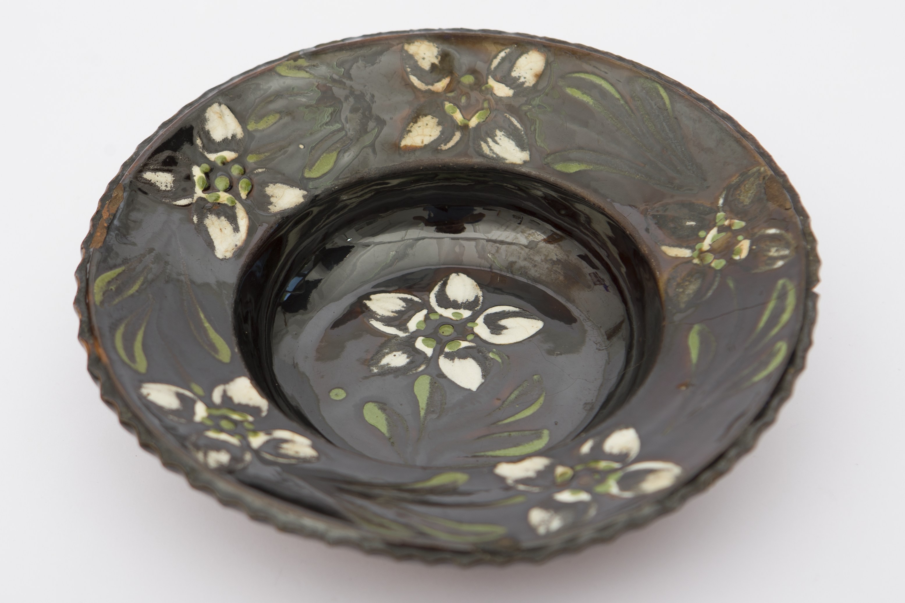 Piesă ceramică smălțuită în interior, de formă tronconică, cu baza plată, marginile puțin evazate și buza vălurită. Peste fondul negru a fost realizat decorul fitomorf stilizat, format din șase flori cu petale albe și frunze verzi. O floare cu puncte verzi în mijloc se află pe fundul vasului. Alte cinci flori, la fel ca cea de pe fundul vasului, în alternanță cu frunze sunt dispuse pe marginea vasului. Pe spate prezintă o ”tortiță” de mici dimensiuni pentru suspendare pe perete. Blidul era folosit pentru servirea hranei, dar și pentru ornamentarea interioarelor. Prezintă uzură funcțională. Cromatică: fond: cărămiziu (exterior); negru (interior); motive: verde; alb.