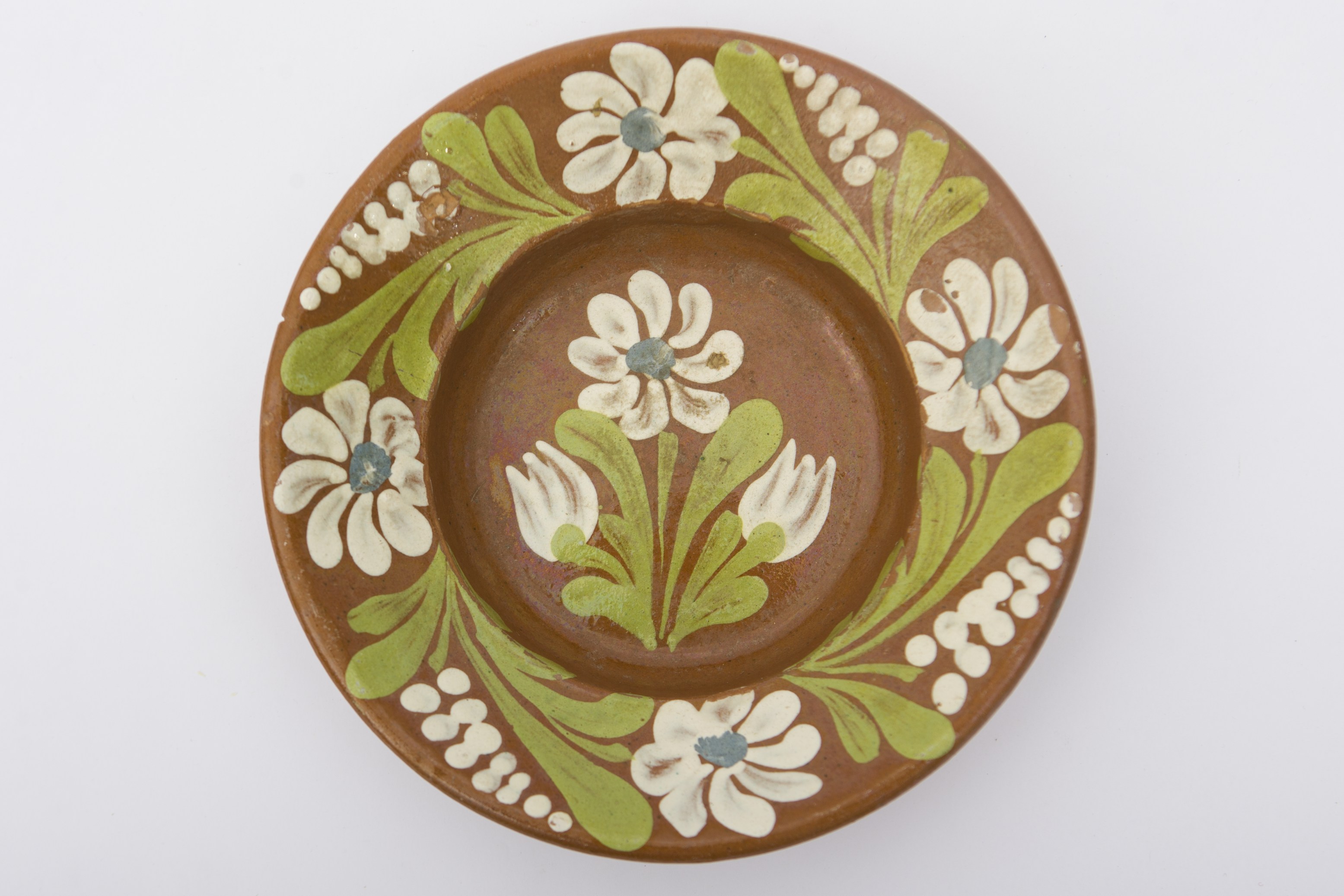 Recipient ceramic smălțuit în interior, de formă tronconică, cu fundul plat, pereții puțin ridicați și marginile ridicate. Pe fond maro deschis, decor fitomorf realizat prin pictare, care ilustrează o alternanță de flori cu petale albe, frunze verzi și motive punctate. Pe fundul vasului se află o floare cu opt petale, un punct albastru în mijloc, încadrată la bază de două flori albe de mici dimensiuni. Patru flori la fel ca cea de pe fundul vasului, în alternanță cu frunze și motive punctate, care se subțiază spre vârf. La spate prezintă o ”tortiță” de mici dimensiuni pentru suspendare pe perete. Blidul era folosit pentru servirea hranei sau decorarea interioarelor. Prezintă uzură funcțională. Cromatică: fond: cărămiziu (exterior); maro deschis (interior); motive: verde; alb; albastru.