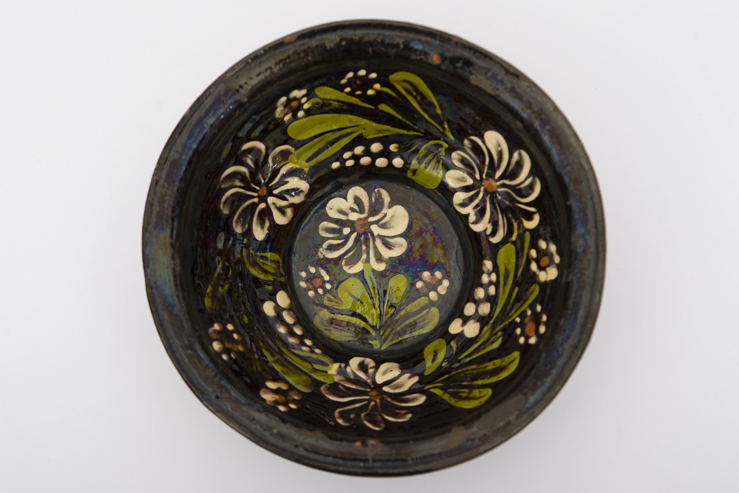 Piesă ceramică de mici dimensiuni, smălțuită în interior, de formă tronconică, cu baza plată, pereții evazați și buza profilată. Pe fondul negru, a fost realizat decorul fitomorf stilizat, reprezentând patru flori cu petale conturate cu alb, un punct maro în centru, frunze verzi, puncte albe dispuse circular ce descriu flori de mici dimensiuni și linii punctate, ce se îngusteză spre vârf. Pe fundul vasului se află o floare încadrată de alte două mai mici. Celelalte trei flori în aceeași alternanță sunt pictate pe marginile vasului. Pe spate prezintă o tortiță de mici dimensiuni pentru suspendare pe perete. Blidul era folosit pentru servirea hranei, dar și pentru ornamentarea interioarelor. Prezintă uzură funcțională. Cromatică: fond: cărămiziu (exterior); negru (interior); motive: verde; maro roșcat; alb.