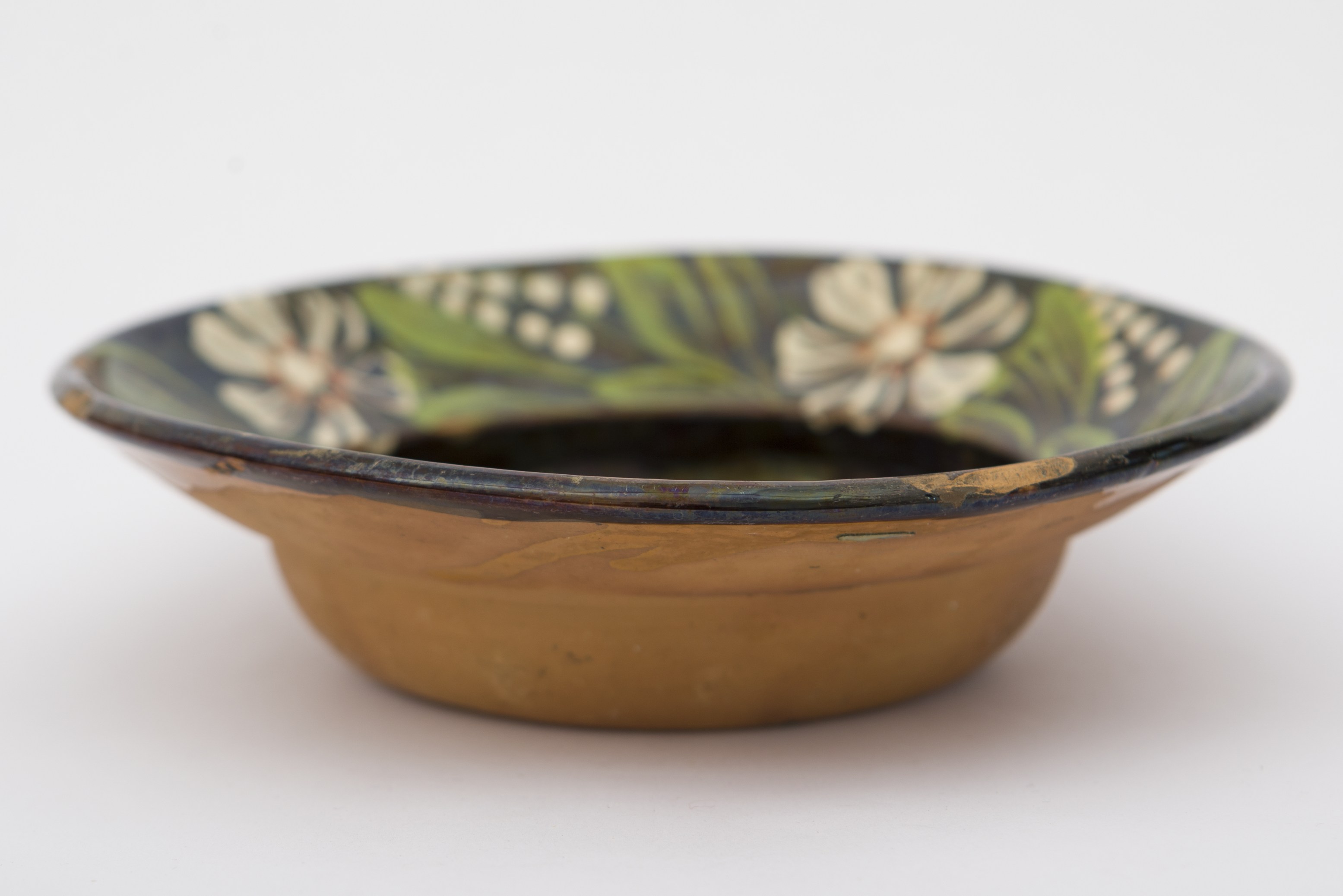 Vas ceramic smălțuit în interior, de formă tronconică, cu marginile puțin ridicate și fundul plat. Pe fond negru decorul fitomorf, reprezentând cinci flori cu petale albe și puncte maro roșcate ce descriu câte un punct în mijloc, frunze lungi verzi și forme punctiforme albe care se subțiază spre vârf. Una dintre flori se află pe fundul vasului, celelalte patru fiind dispuse concentric pe marginea vasului. Pe spate prezintă o tortiță de mici dimensiuni pentru suspendare pe perete. Blidul folosea la decorarea interioarelor. Prezintă uzură funcțională. Cromatică: fond: cărămiziu (exterior); negru (interior); motive: verde; alb; maro roșcat.