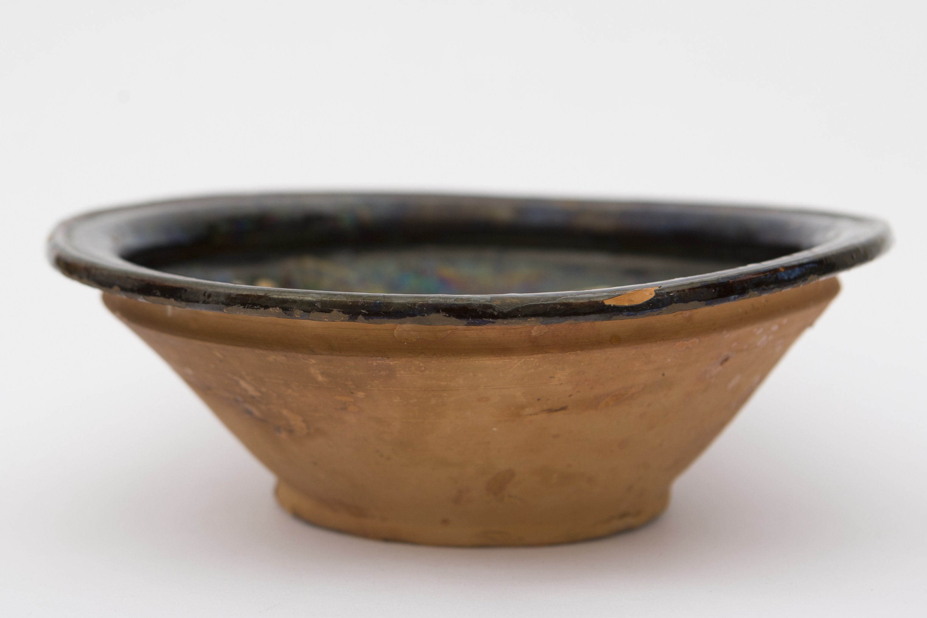 Recipient ceramic de mici dimensiuni, smălțuit la interior, de formă tronconică, cu baza plată, pereții evazați și buza profilată. Pe fond negru, a fost realizat decorul fitomorf stilizat, reprezentând patru flori cu petale albe, frunze verzi, linii punctate, ce se subțiază spre vârf și sunt dispuse câte două de-a lungul fiecărei tulpini. O floare încadrată de câte două grupuri de puncte ce descriu fiecare câte o floare cu un punct maro, în mijloc. Celelalte trei flori dispuse circular pe același registru pe marginile vasului. Pe spate prezintă o ”tortiță” de mici dimensiuni pentru suspendare pe perete. Blidul era folosit pentru servirea hranei, dar și pentru ornamentarea interioarelor. Prezintă uzură funcțională. Cromatică: fond: cărămiziu (exterior); negru (interior); motive: verde; maro roșcat; alb.