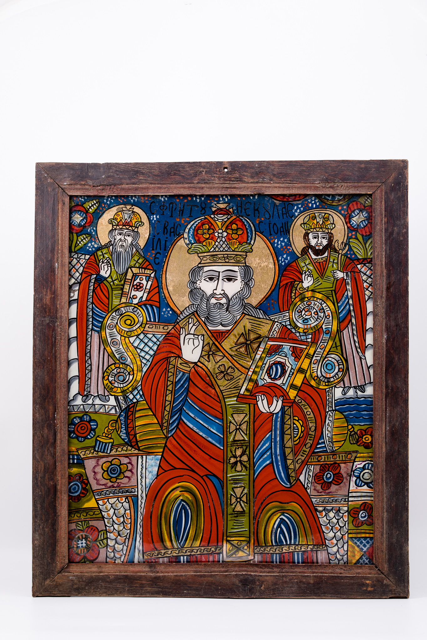 Sfântul Mare Ierarh Nicolae, făcător de minuni, îmbrăcat în veșminte liturgice, de ierarh, sacos albastru, felon roșu vermillon, cu interiorul galben-albastru și epitrahil-patrafir brun-bronziu, cu șase cruci negre brodate. Ține în mâna stângă Sfânta Evanghelie închisă și cu mâna dreaptă Binecuvântează. Este unul dintre cei mai populari și iubiți sfinți, ocrotitor al caselor, familiilor și copiilor. Are barbă sură și mithră arhierească și aureolă. În registrul superior, sunt Sfântul Ierarh Vasile cel Mare și Sfântul Ierarh Ioan Gură-de-Aur Binecuvântând, stând cu picioarele pe mandorle de nouri albi-gri. Fondul este cerul albastru cobalt-regal, bogat în elemente punctiflorale albe și roșii, în registrul superior și policrom în câmpuri alternativ-paralele, bogat în elemente decorative florale, în registrul inferior. Tronul arhieresc este bogat ornamentat cu elemente decorative bronzii și albastru-galben cu roz-stacojiu. Desenul este fin conturat. Cromatica este armonioasă: roșu vermillon, roz-stacojiu, albastru regal și cobalt, bronz, brun, bej, crem, auriu, alb, negru. Inscripția din româno-chirilică se traduce Sfântul Nicolae Sf Vasile Sf Ioan. Icoana este din Țara Oltului și este mai rară, datorită prezențelor Sfântului Vasile cel Mare și a Sfântului Ioan Gură-de-Aur.