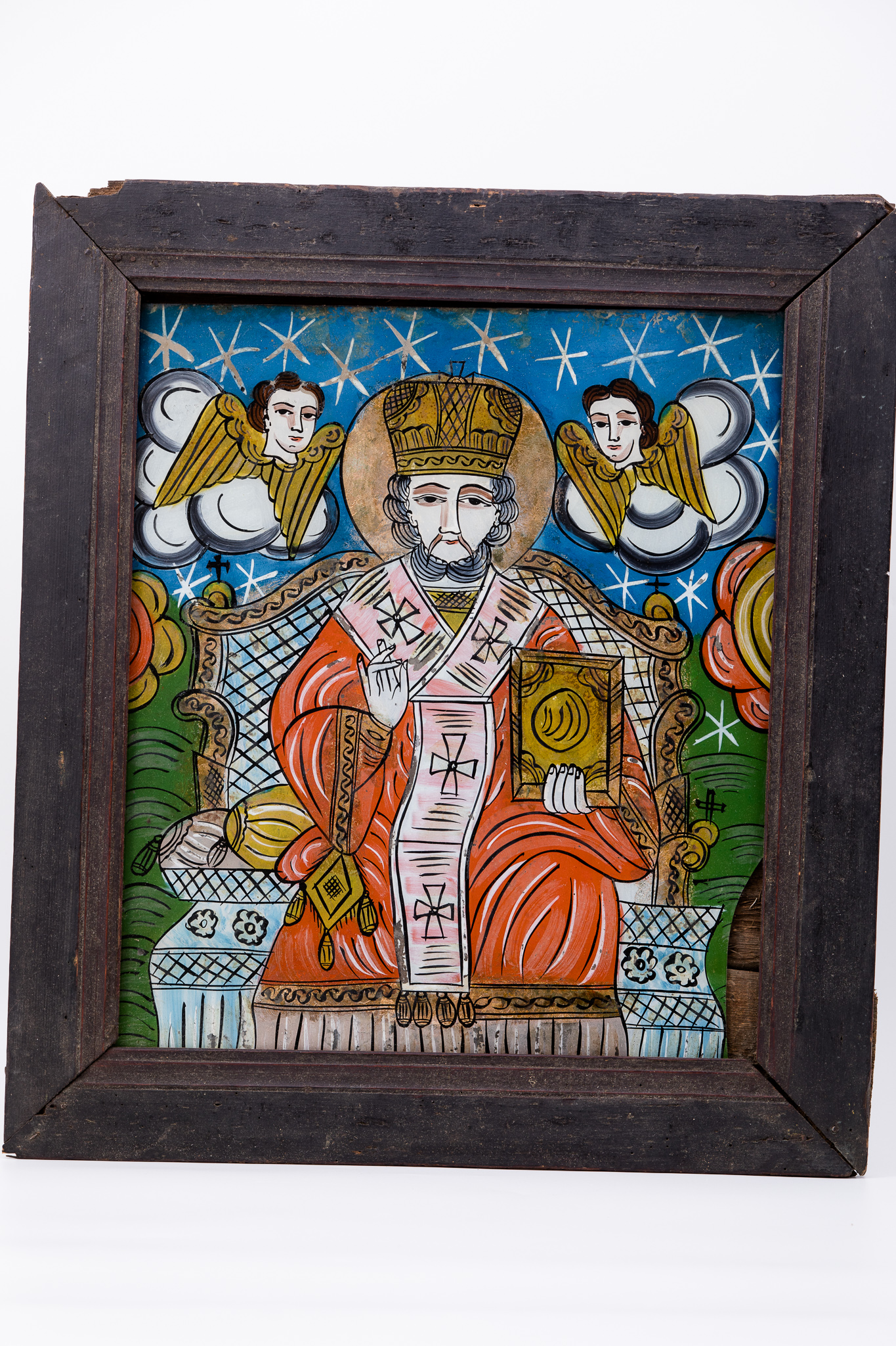 Sfântul Mare Ierarh Nicolae, făcător de minuni, îmbrăcat în veșminte liturgice, de ierarh, sacos și felon roșu vermillon-cărămiziu, cu epitrahil-patrafirul roz-putred stacojiu, cu patru cruci brune brodate. Ține în mâna stângă Sfânta Evanghelie închisă și cu mâna dreaptă Binecuvântează. Este unul dintre cei mai populari și iubiți sfinți, ocrotitor al caselor, familiilor și copiilor. Are barbă albă-sură și mithră arhierească și aureolă. În registrul superior, sunt doi îngeri serafimi, cu aripile galbene-ocru, pe mandorle de nouri rotunzi alb-gri. Fondul icoanei este cerul albastru regal, bogat în elemente astrale - stele albe, în registrul superior și câmpuri verzi-văratice, cu două elemnte florale supradimensionate, floare roșie cu miezul-pistilul galben, în registrul inferior. Tronul arhieresc este bogat ornamentat cu elemente decorative bronzii și albastre bleu-ciel senin. Desenul este fin conturat. Cromatica este armonioasă: roșu vermillon, roz putred-stacojiu, albastru regal și bleu-ciel, galben-ocru, verde văratic, bronz, brun, bej, crem, auriu, alb, negru. Icoana este de Țara Oltului