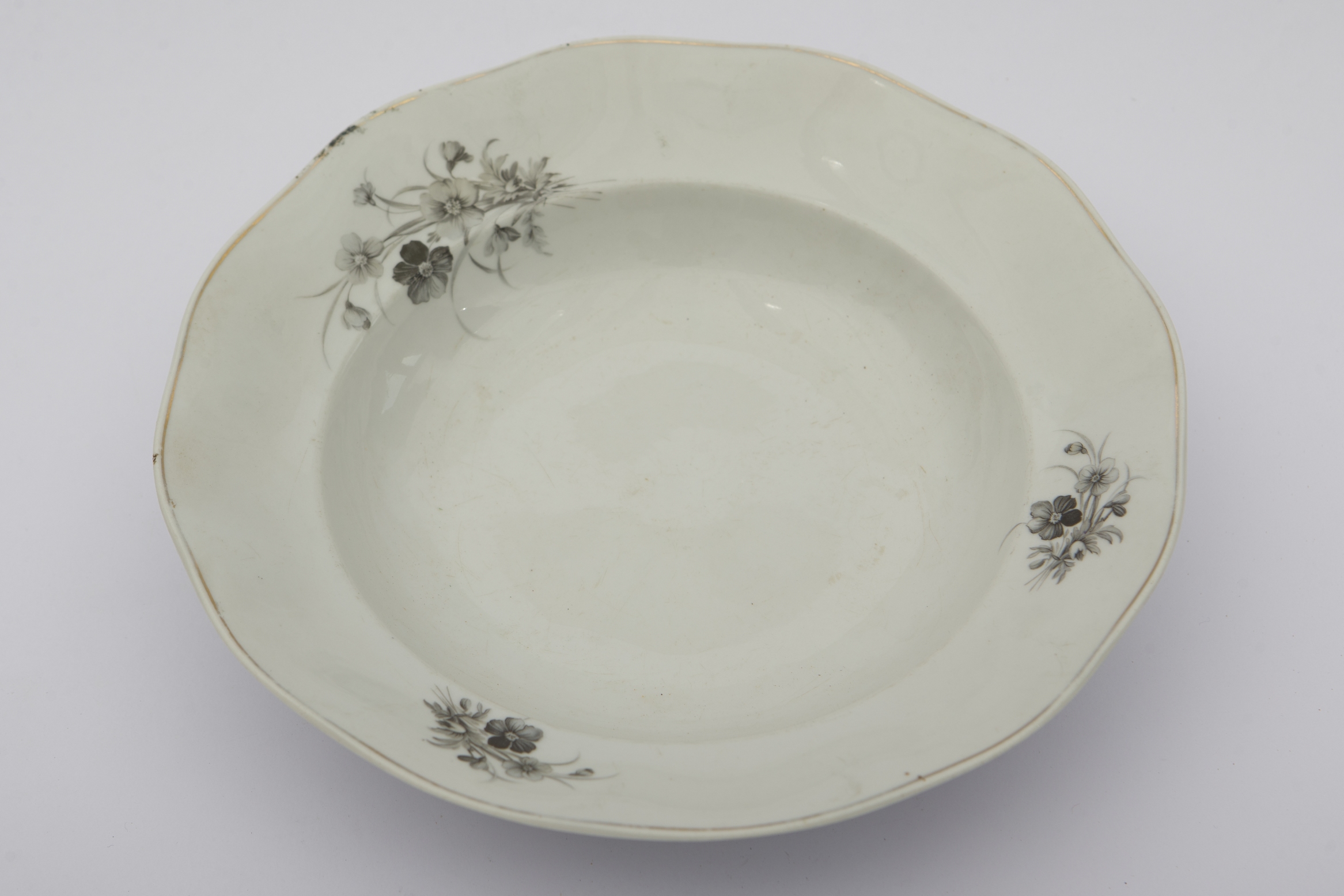 Vas ceramic smălțuit, de formă rotundă și cu marginile puțin ridicate și fundul plat. Marginile vasului puțin ondulate. Pe fond alb trei compoziții floral-vegetale dispuse pe marginile vasului, având culoarea neagră. Buza piesei a fost conturată cu o linie circulară aurie. Farfuria era folosită în gospodărie pentru servirea hranei. Prezintă uzură funcțională. Cromatică: fond: alb; motive: negru.