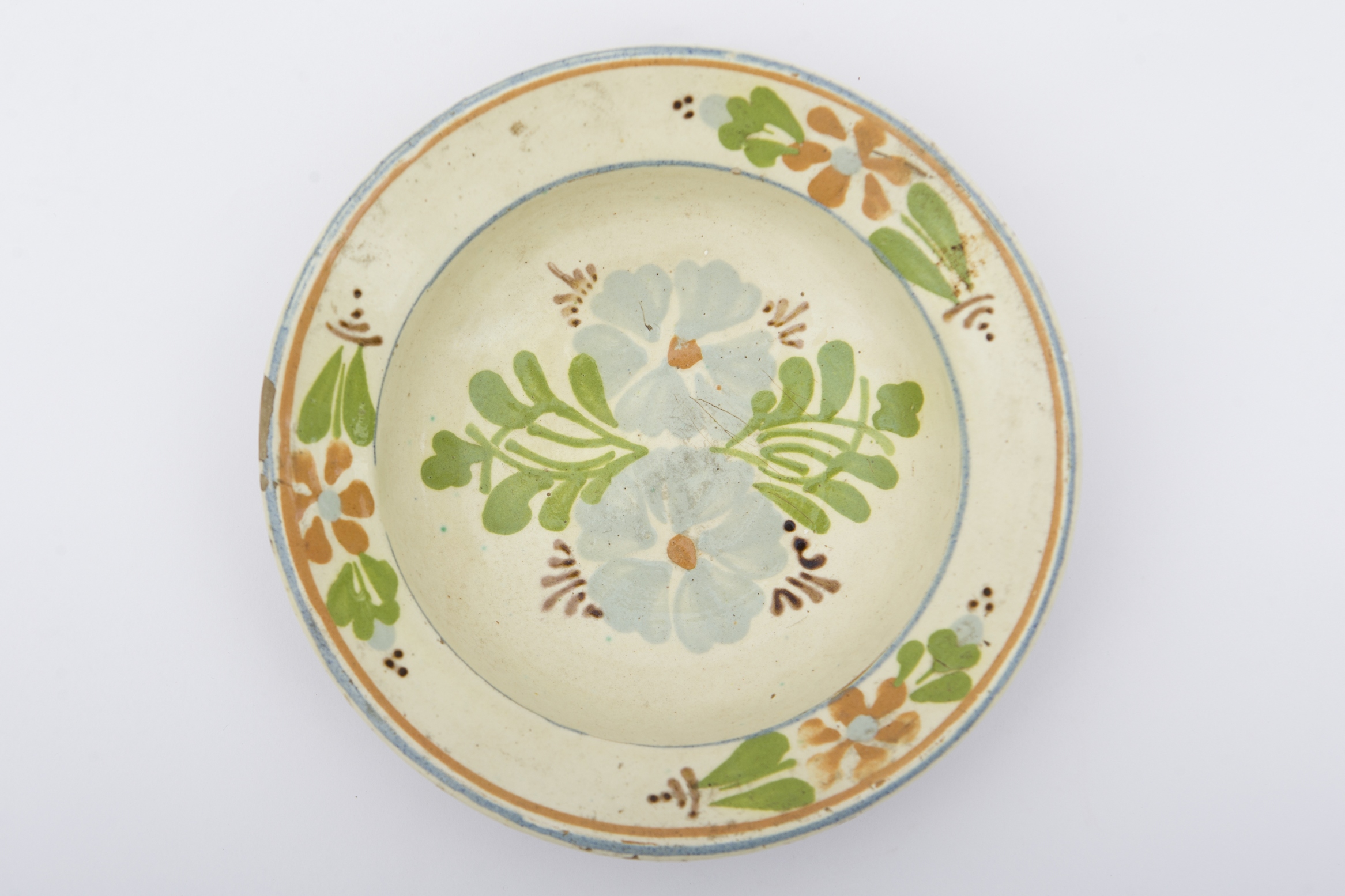 Vas ceramic de mici dimenisuni, având formă tronconică, cu baza plată, pereții ușor ridicați și marginile evazate. Peste fondul alb de angobă a fost realizat decorul geometrizant și fitomorf stilizat. Central, pe fundul vasului sunt dispuse două flori albastre cu mijlocul maro roșcat, fiind mărginite de frunze verzi. Marginile vasului au fost ornamentate cu trei grupuri, formate din flori maro, cu mijlocul albastru și frunze verzi, încadrate între două linii circulare albastre. Pe spate prezintă două orificiii pentru suspendare. Blidul era folosit pentru servirea hranei sau ornamentarea interioarelor. Prezintă uzură funcțională. Cromatică: fond: cărămiziu (exterior); alb (interior); motive: albastru; verde; maro roșcat; maro închis.