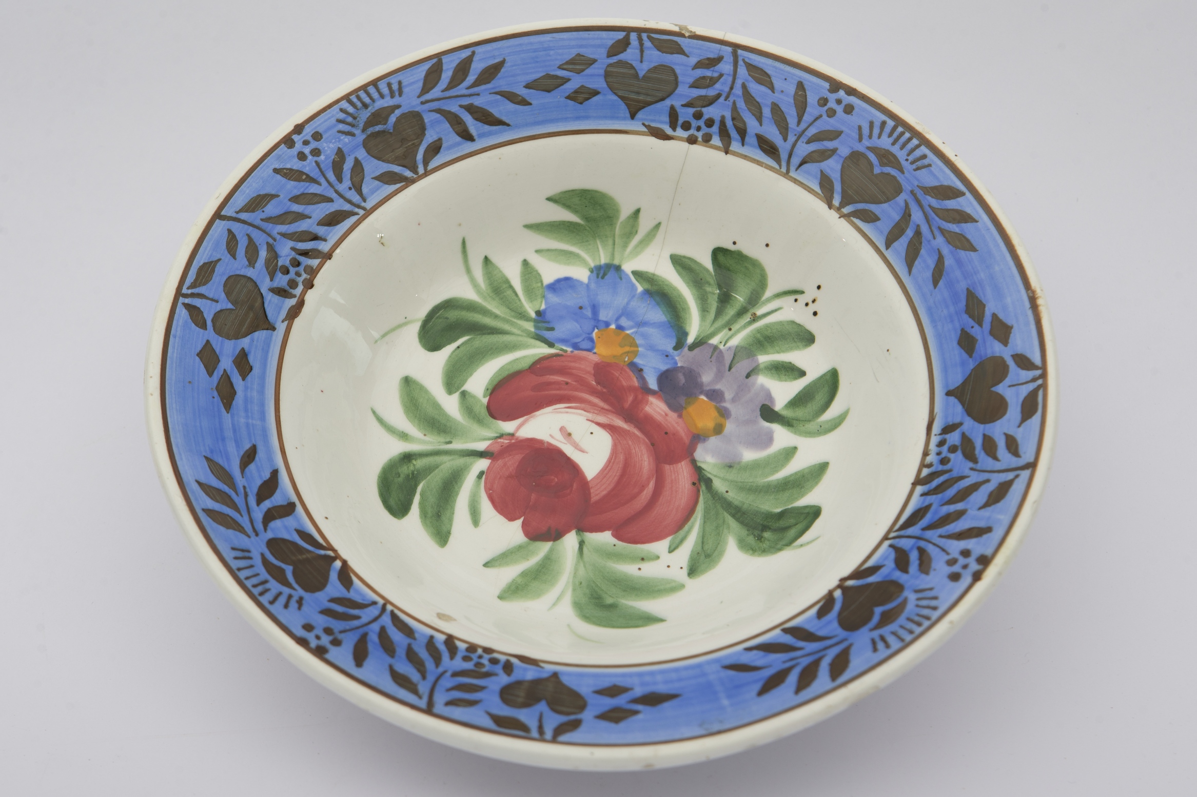 Piesă ceramică smălțuită, de formă circulară, cu baza plată, marginile puțin ridicate și buza evazată. Pe fond alb au fost pictate decorații în registru fitomorf, ilustrând o compoziție formată dintr-un trandafir roșu și două flori de dimensiuni mai reduse (una albastră și una mov), fiecare cu câte un punct portocaliu. Registrul de pe fundul vasului a fost completat cu frunze verzi. Marginile vasului conturate de două linii circulare negre, pe fond albastru, au fost ornamentate cu motive geometrizante și fitomorfe diverse: flori, romburi, inimioare. Pe spate, bază prezintă două perforații pentru suspendare. Farfuria era folosită în gospodărie pentru servirea hranei sau decorarea interioarelor. Prezintă uzură funcțională. Cromatică: fond: alb; motive: albastru; verde; roșu; mov; negru; portocaliu.