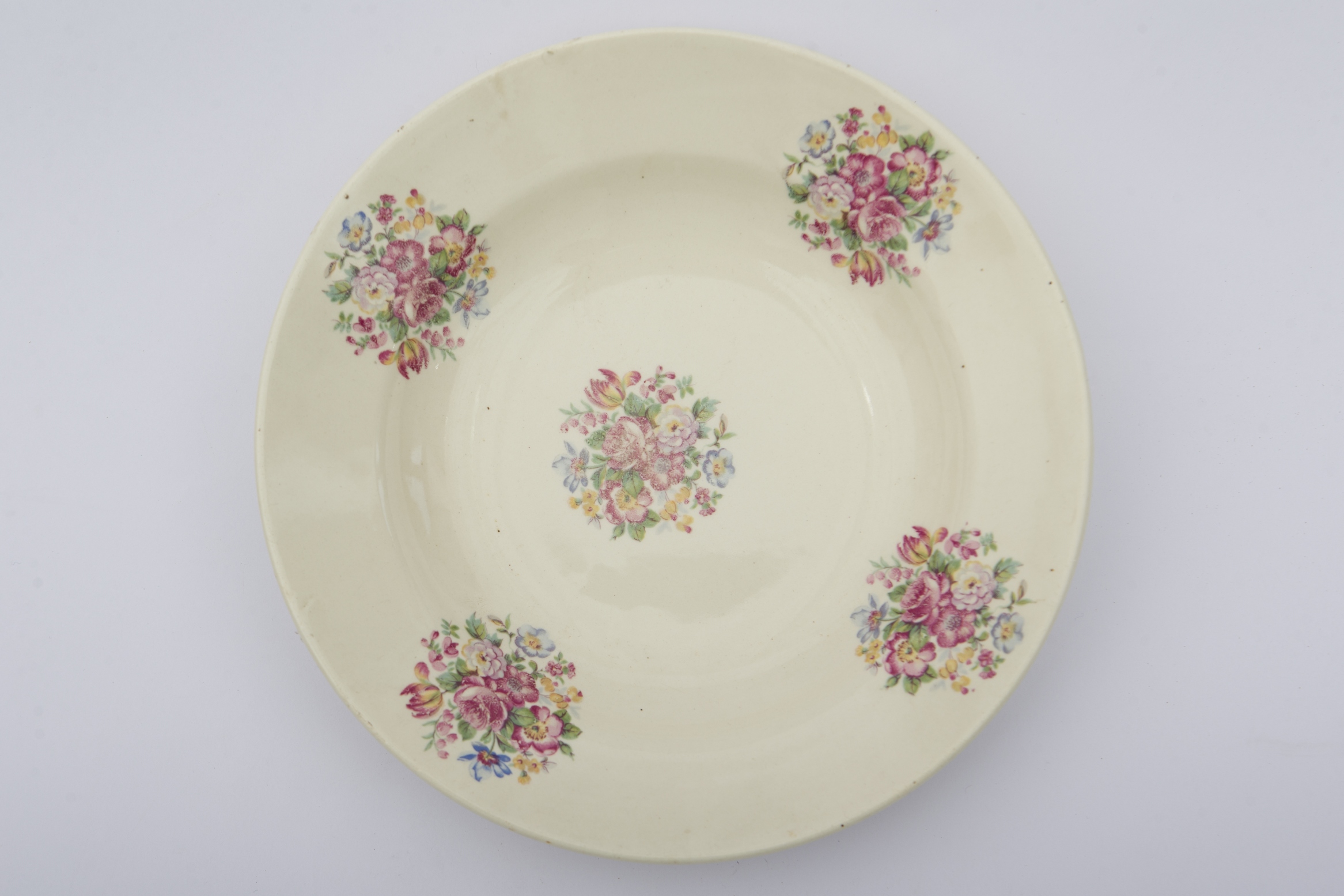 Vas ceramic smălțuit, de formă rotundă, cu baza plată susținută de un inel, pereții ușor ridicați și buza profilată. Peste fondul alb au fost pictate decorații fitomorfe, ilustrând cinci compoziții din flori policrome. Pe spate au fost săpate două orificii pentru fixarea pe perete sau blidar. Farfuria era folosită pentru servirea hranei sau ornamentarea interioarelor. Prezintă uzură funcțională. Cromatică: fond: alb; motive: roz; albastru; verde; galben.