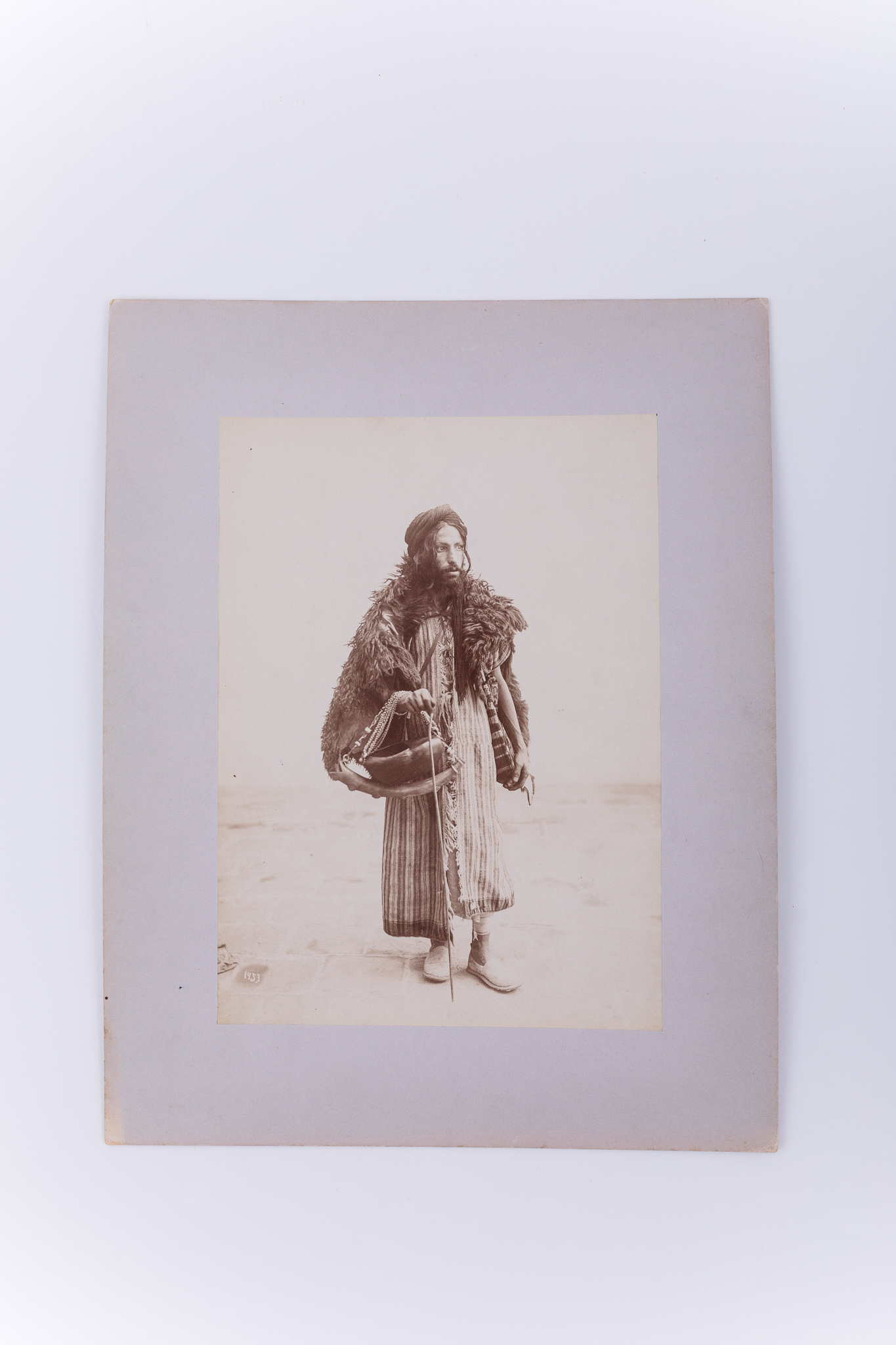 Fotografie de atelier ce prezintă un bărbat dervish ce are în mână un vas pentru cerșit. Imaginea este realizată pe hârtie albuminată, după un clișeu pe sticlă și este lipită pe un carton gros, de culoare gri. Pe clișeu, însemnare manuscrisă cu numărul clișeului „1453” (practică frecventă în opera lui Antoin Sevruguin). Aceeași imagine apare în „Myron Bement Smith Collection”, din cadrul „National Museum of Asian Art” (muzeul american deține o reproducere pe hârtie cu gelatino-bromură de argint realizată de Joseph Upton). Fotografia din colecția Muzeului ASTRA face parte dintr-un album ce conține 51 de piese, realizate pe hârtie albuminată, aparținând lui Antoin Sevruguin. Acestea prezintă tipuri umane, peisaje și arhitectura din Iran de la sfârșitul secolului al XIX lea și începutul secolului al XX lea, în perioada dinastiei Qajar. Pe coperta albumului, confecționat din imitație de piele roșie, apare textul „Teheran” realizat cu tuș auriu, prin presare, încadrat într-un paspartu cu modele persane, realizat tot prin presare. Pe verso, însemnare manuscrisă, în limba germană, parțial descifrabilă: „Nr. 33. / ...”; ștampilă: Muzeul „Brukenthal” Sibiu / Nr. ...; număr de inventar MCPR 2268.