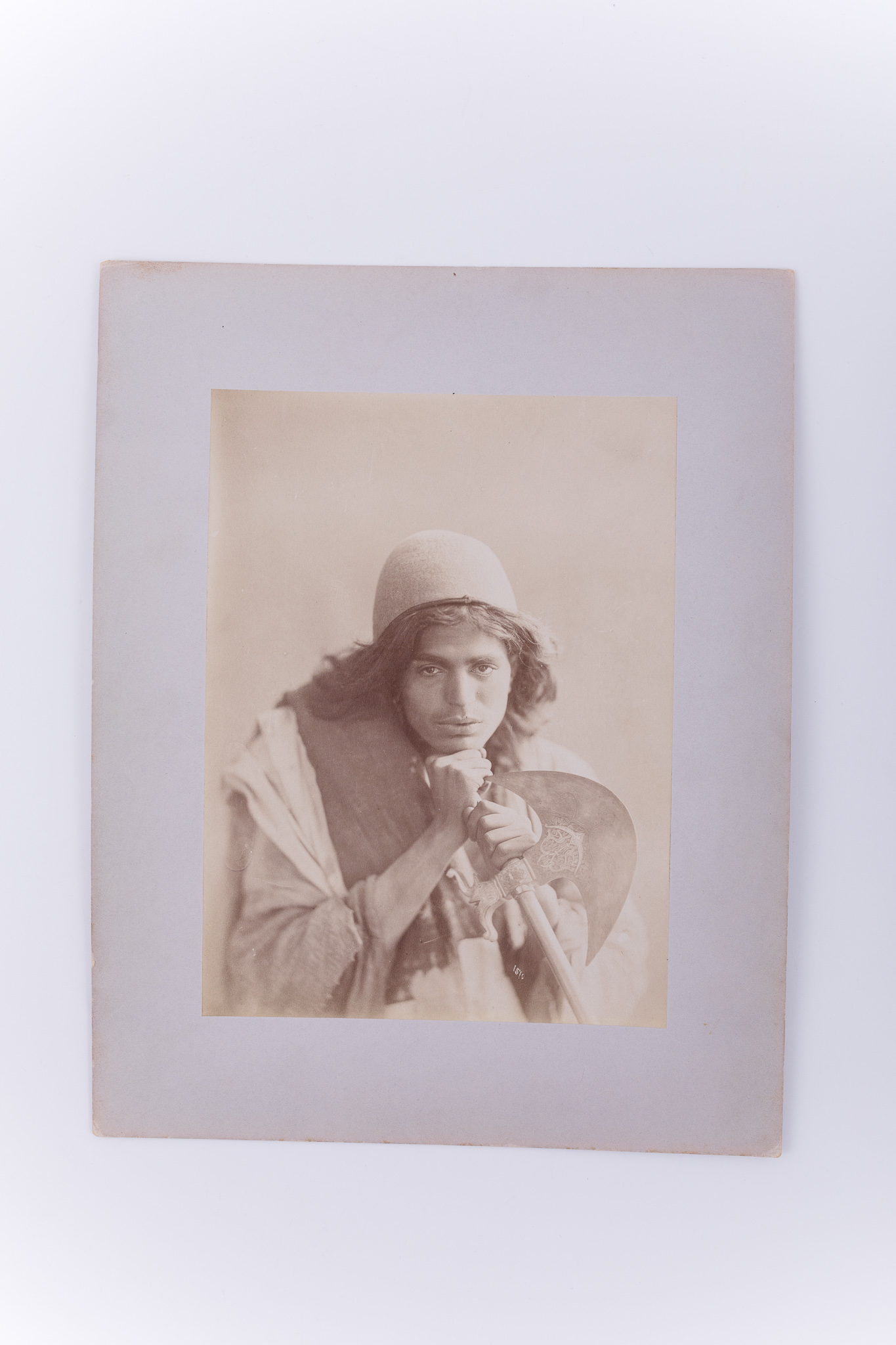 Fotografie de atelier ce prezintă un băiat dervish ce ține în mână o secure cu modele orientale. Imaginea este realizată pe hârtie albuminată, după un clișeu pe sticlă și este lipită pe un carton gros, de culoare gri. Pe clișeu, însemnare manuscrisă cu numărul clișeului, „1570” (practică frecventă în opera lui Antoin Sevruguin). Fotografia din colecția Muzeului ASTRA face parte dintr-un album ce conține 51 de piese, realizate pe hârtie albuminată, aparținând lui Antoin Sevruguin. Acestea prezintă tipuri umane, peisaje și arhitectura din Iran de la sfârșitul secolului al XIX lea și începutul secolului al XX lea, în perioada dinastiei Qajar. Pe coperta albumului, confecționat din imitație de piele roșie, apare textul „Teheran” realizat cu tuș auriu, prin presare, încadrat într-un paspartu cu modele persane, realizat tot prin presare. Pe verso, însemnare manuscrisă, în limba germană, parțial descifrabilă: „Nr. 23. / …”; ștampilă: Muzeul „Brukenthal” Sibiu / Nr. ….; număr de inventar MCPR 2266.