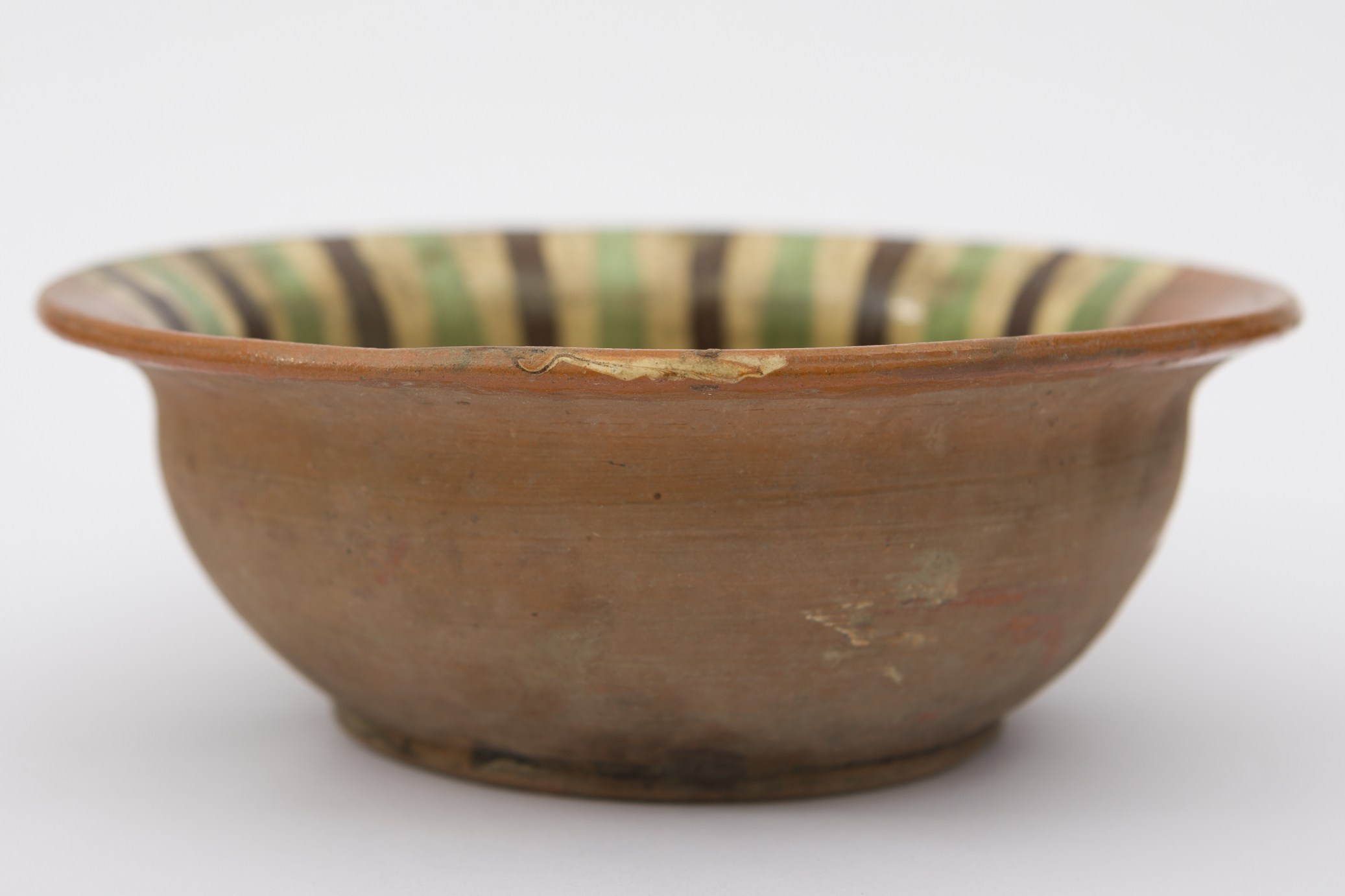 Recipient ceramic smălțuit de dimensiuni medii, având formă tronconică, cu baza plată, pereții evazați și buza răsfrântă. Întreaga suprafață interioară a strachinei a fost decorată cu motive decorative picturale. Peste stratul maro roșcat de angobă au fost realizate motive geometrizante: benzi de culoare verde, negru, galben intercalate, fiind îngustate în partea inferioară. Srachina era folosită în gospodărie pentru manevrarea sau servirea hranei. Prezintă uzură funcțională. Cromatică: fond: cărmiziu roșcat; motive: verde; negru; galben.