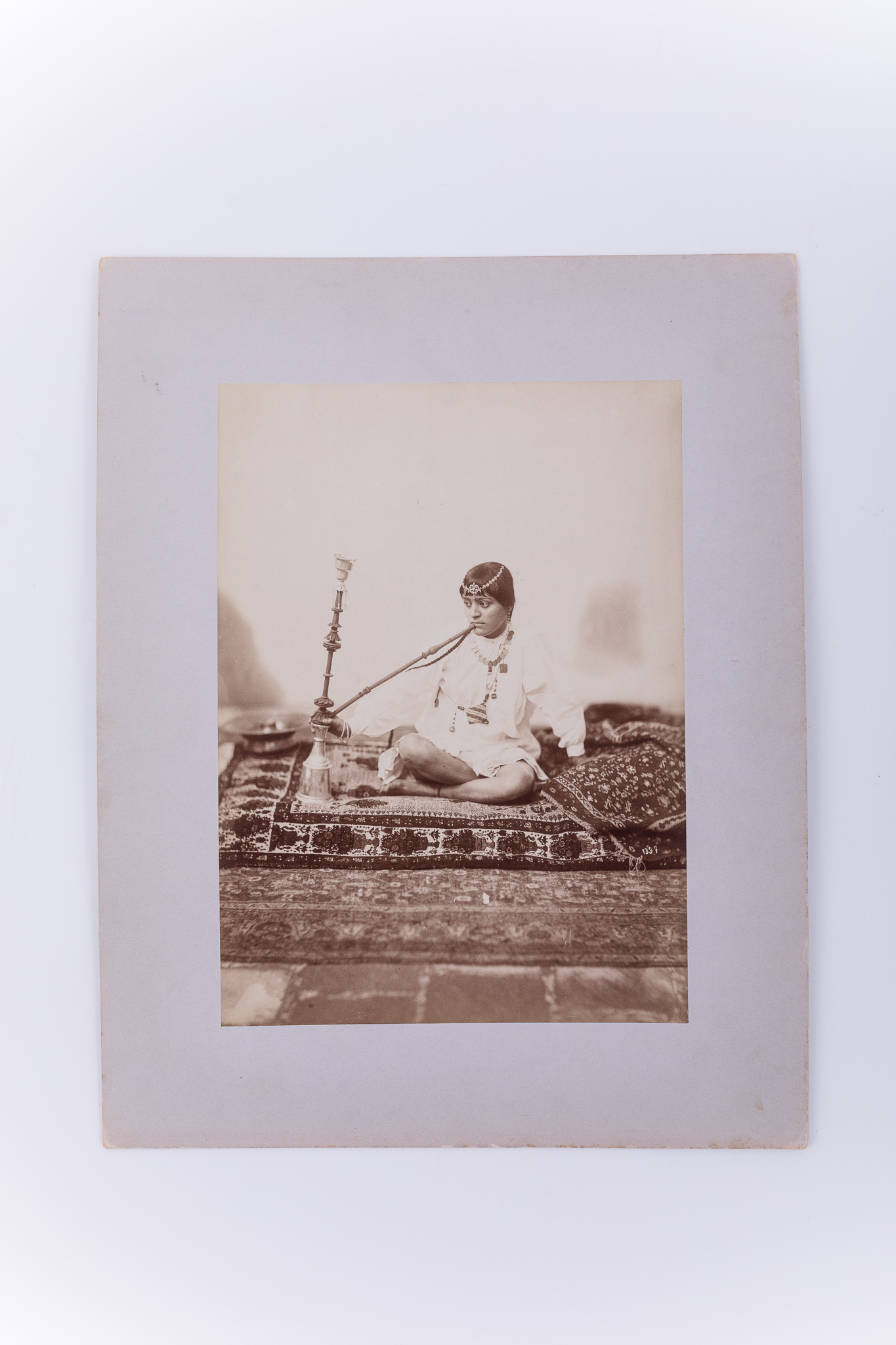 Fotografie de atelier ce prezintă o femeie așezată pe covor și care fumează dintr-o pipă cu apă. Imaginea este realizată pe hârtie albuminată, după un clișeu pe sticlă și este lipită pe un carton gros, de culoare gri. Pe clișeu, însemnare manuscrisă cu numărul clișeului „1337” (practică frecventă în opera lui Antoin Sevruguin). Aceeași imagine apare în „The Nelson Collection of Qajar Photography”. Fotografia din colecția Muzeului ASTRA face parte dintr-un album ce conține 51 de piese, realizate pe hârtie albuminată, aparținând lui Antoin Sevruguin. Acestea prezintă tipuri umane, peisaje și arhitectura din Iran de la sfârșitul secolului al XIX lea și începutul secolului al XX lea, în perioada dinastiei Qajar. Pe coperta albumului, confecționat din imitație de piele roșie, apare textul „Teheran” realizat cu tuș auriu, prin presare, încadrat într-un paspartu cu modele persane, realizat tot prin presare. Pe verso, însemnare manuscrisă, în limba germană, parțial descifrabilă: „Nr. 35. / …”; ștampilă: Muzeul „Brukenthal” Sibiu / Nr. ....; număr de inventar MCPR 2283.