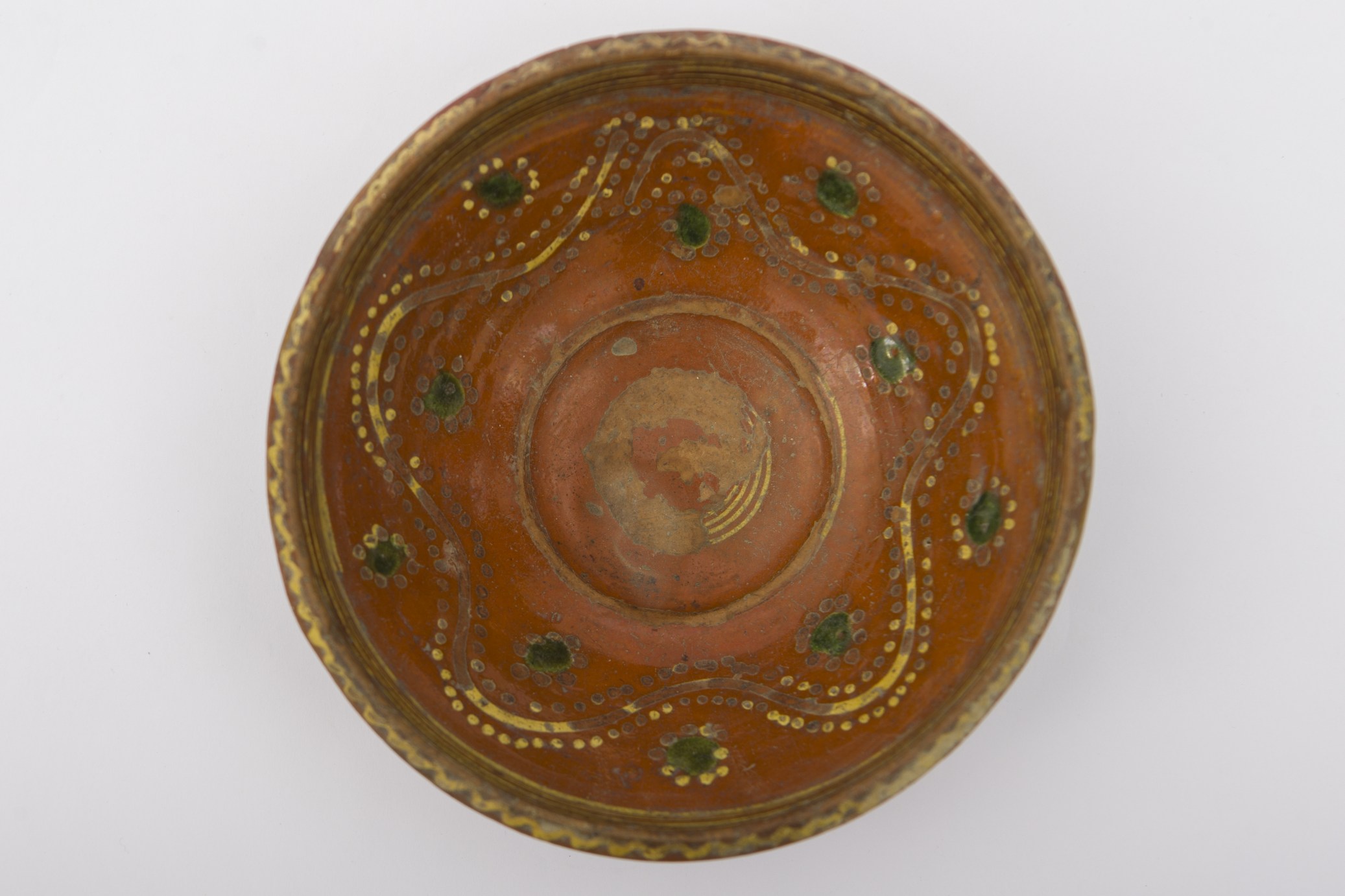 Vas ceramic smălțuit de mici dimensiuni, de formă tronconică, cu baza plată, pereții înalțați și buza evazată. Interiorul strachinei a fost ornamentat cu motive geometrizante și fitomorfe stilizate. Central, pe fundul vasului au fost pictate cinci linii concentrice. Pereții au fost la rândul lor decorați cu trei linii vălurite: două linii punctate, încadrează cea de-a treia linie continuă. De-o parte și alta a grupului de linii, au fost pictate zece flori cu mijlocul verde și frunze galbene. Alte patru linii drepte sunt dispuse circular pe interiorul buzei. Strachina era folosită în gospodărie pentru servirea hranei. Prezintă uzură funcțională. Cromatică: fond: maro roșcat; motive: galben; verde.