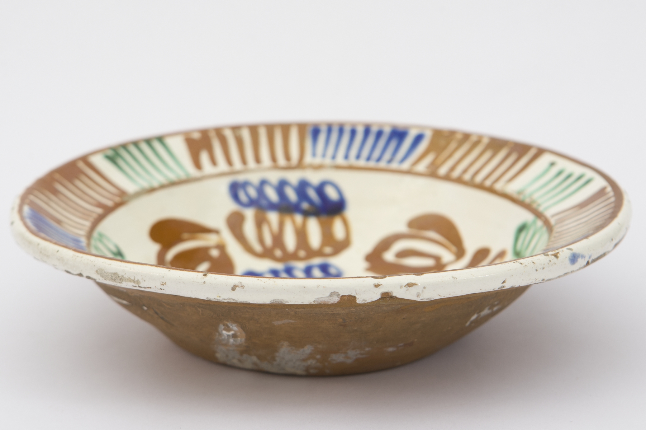 Vas ceramic smălțuit, de mici dimensiuni, având formă tronconică, cu baza neprofilată, pereții înalți și buza oblică și puternic evazată. Farfuria prezintă la nivelul suprafeței interioare, peste stratul alb de angobă, motive fitomorfe și geometrizante stilizate. Astfel, primul registru pictural, dispus pe fundul vasului este format din motive florale, cu frunzele (verzi și albastre) și tulpina (maro roșcat) spiralate, care prezintă la unul din capete boboci de floare. Marginal, pe buza piesei au fost realizat grupuri de linii verticale succesive, de diferite culoari (maro roșcat, albastru, verde), încadrate de două linii circulare drepte. Farfuria era folosită în gospodărie pentru decorarea interioarelor sau pentru servirea hranei. Prezintă uzură funcțională. Cromatică: fond: cărămiziu; alb; motive: maro roșcat; albastru; verde.