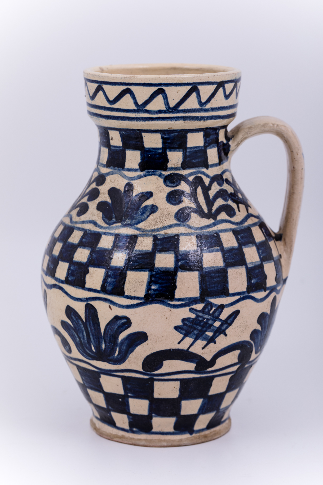 Cană piriformă prevăzută cu o toartă dreaptă și lată, gura rotundă. Suprafața decorativă a vasului este împărțită în șase registre decorative: cel din partea superioară, pe buza vasului este dispus orizontal, iar celelalte cinci, dispuse vertical. Primul registru, așezat pe marginea dreaptă a cănii redă o linie vălurită. Registrul al doilea, al patrulea și al șaselea prezintă motivul tablei de șah. Al treilea și cincelea redă motivul pomului vieții și motive fitomorfe stilizate, intercalate de o lalea înflorită cu cinci petale. Toarta este decorată cu două grupuri de motive care reprezintă linii intersectate. Piesa este ștampilată pe fundul vasului cu marca atelierului mecanizat Bordon de la Petrești și reprezintă o bufniță și inscripția „Siebenburgen”. Piesa este o replică a ceramicii de Drăușeni.